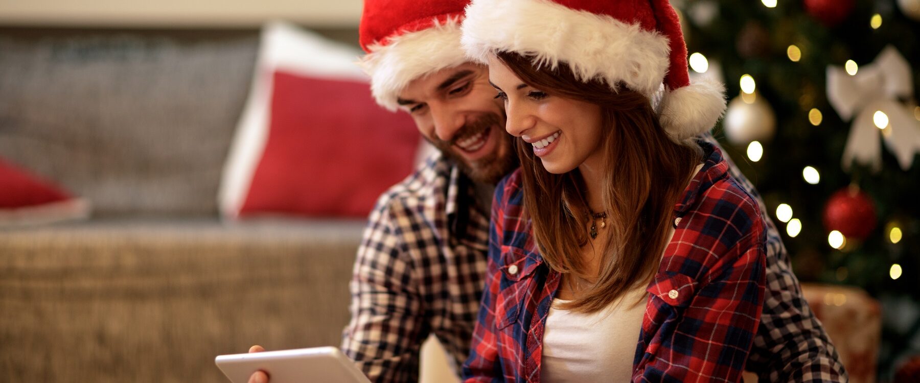 Zwei glückliche Menschen mit Weihnachtsmütze schauen auf einen Bildschirm