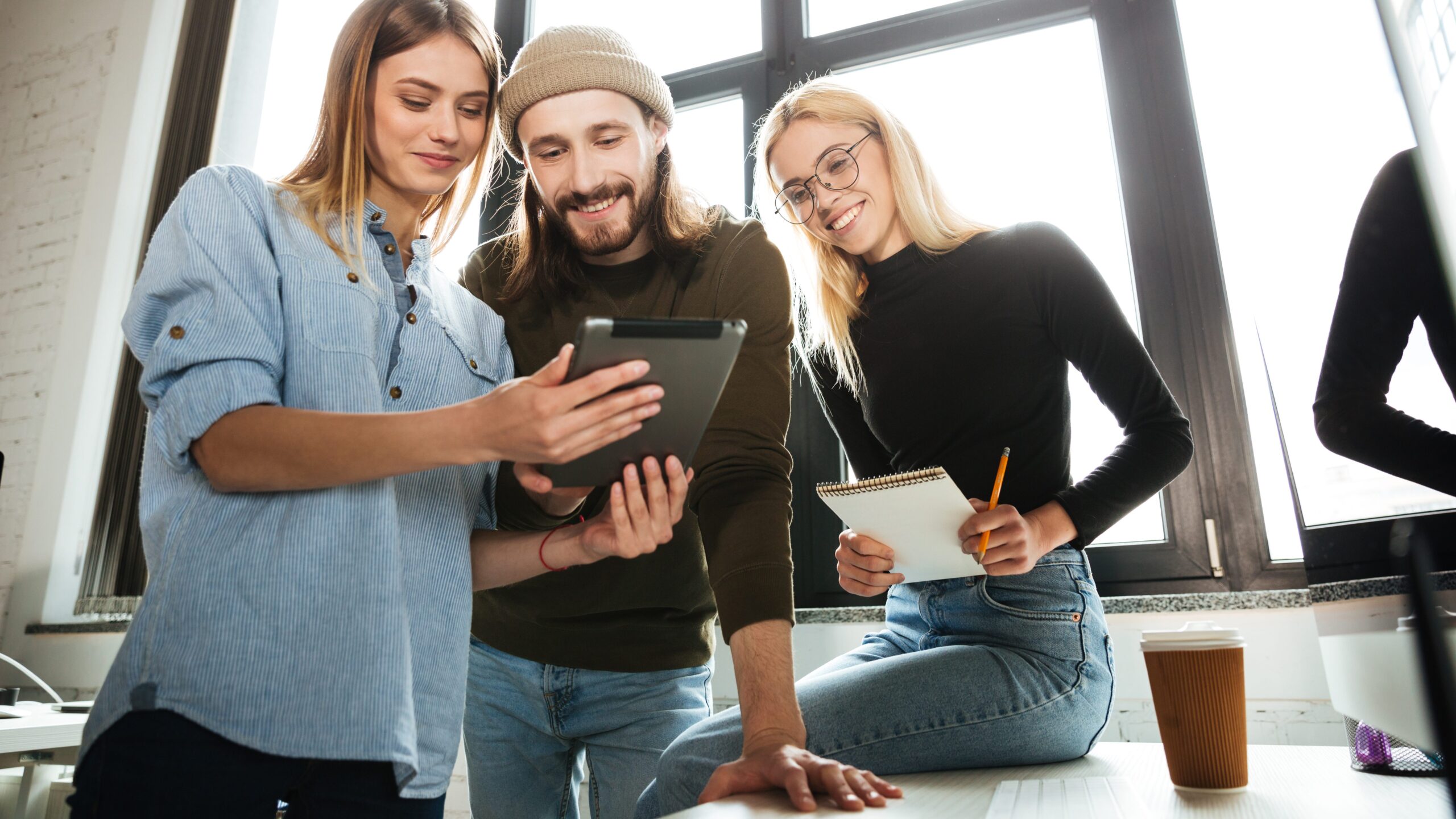 Ein junger Mann und zwei junge Frauen schauen gemeinsam auf ein Tablet.