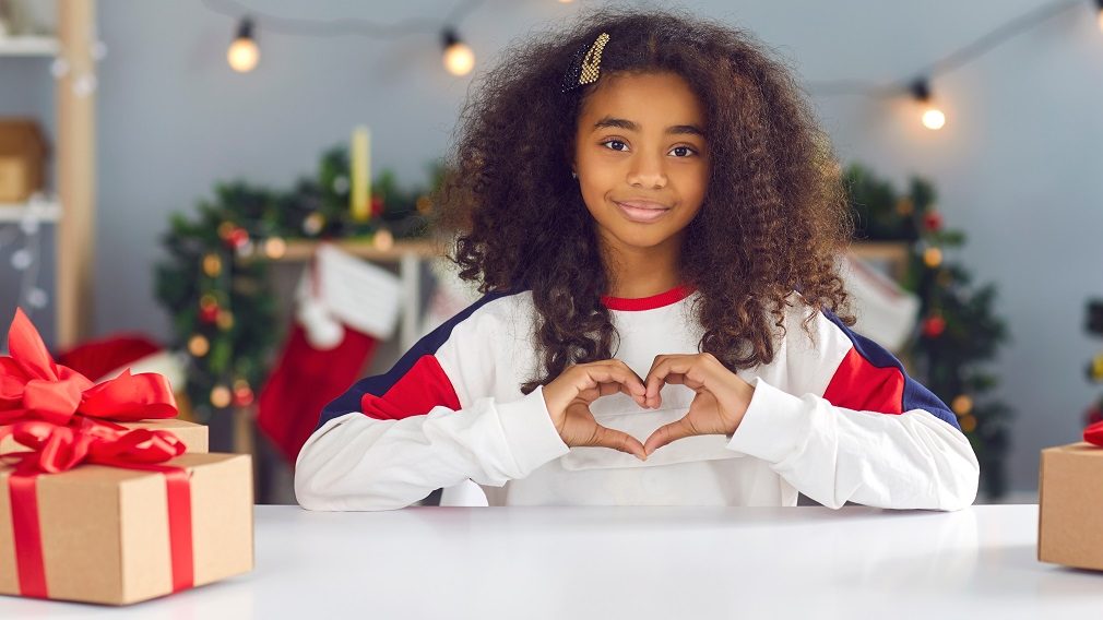 Mädchen zeigt Herz mit Händen an Tisch mit Weihnachtsdeko