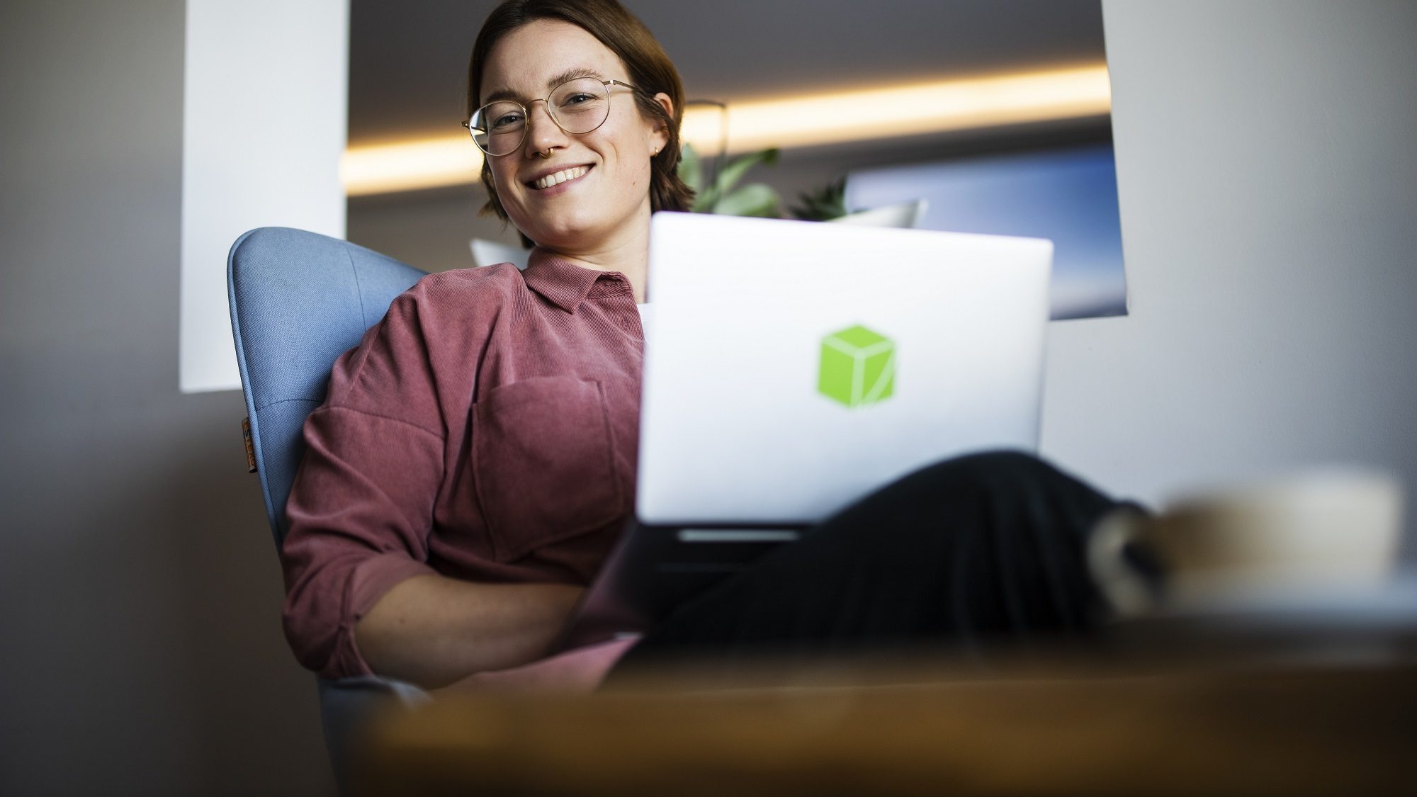 Frau mit Laptop auf Schoß lächelt in die Kamera