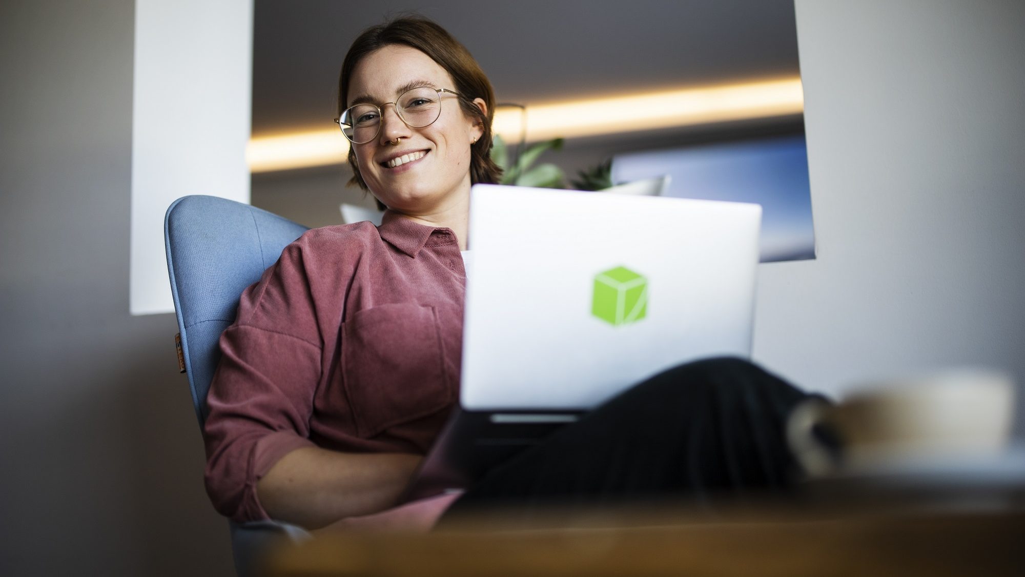 Frau mit Laptop auf Schoß lächelt in die Kamera