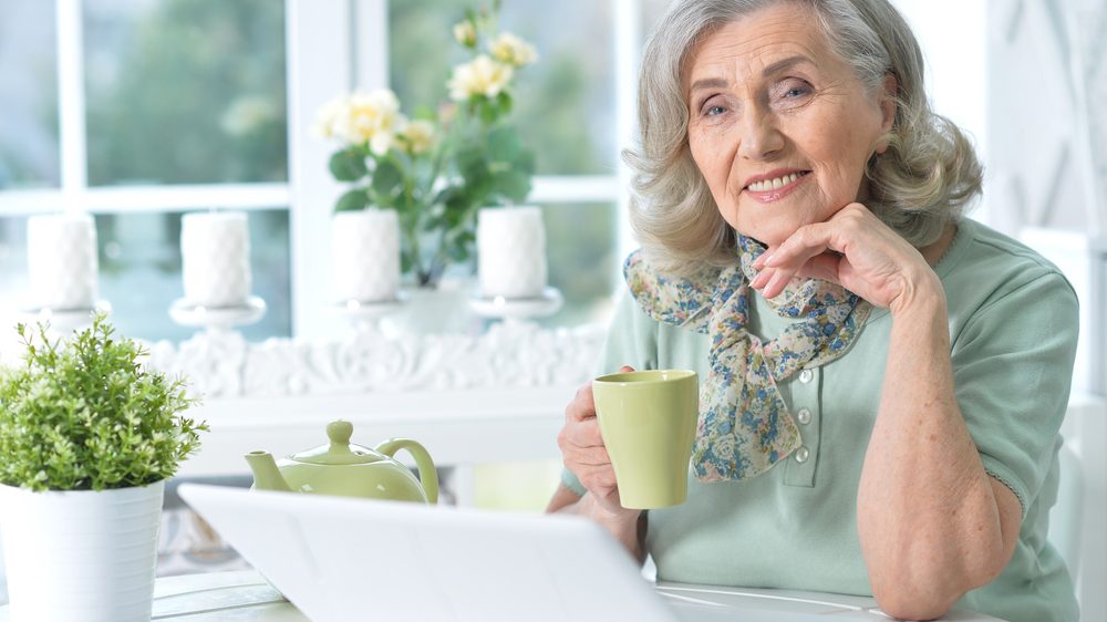 Seniorin sitzt lächelnd vor einem LapTop