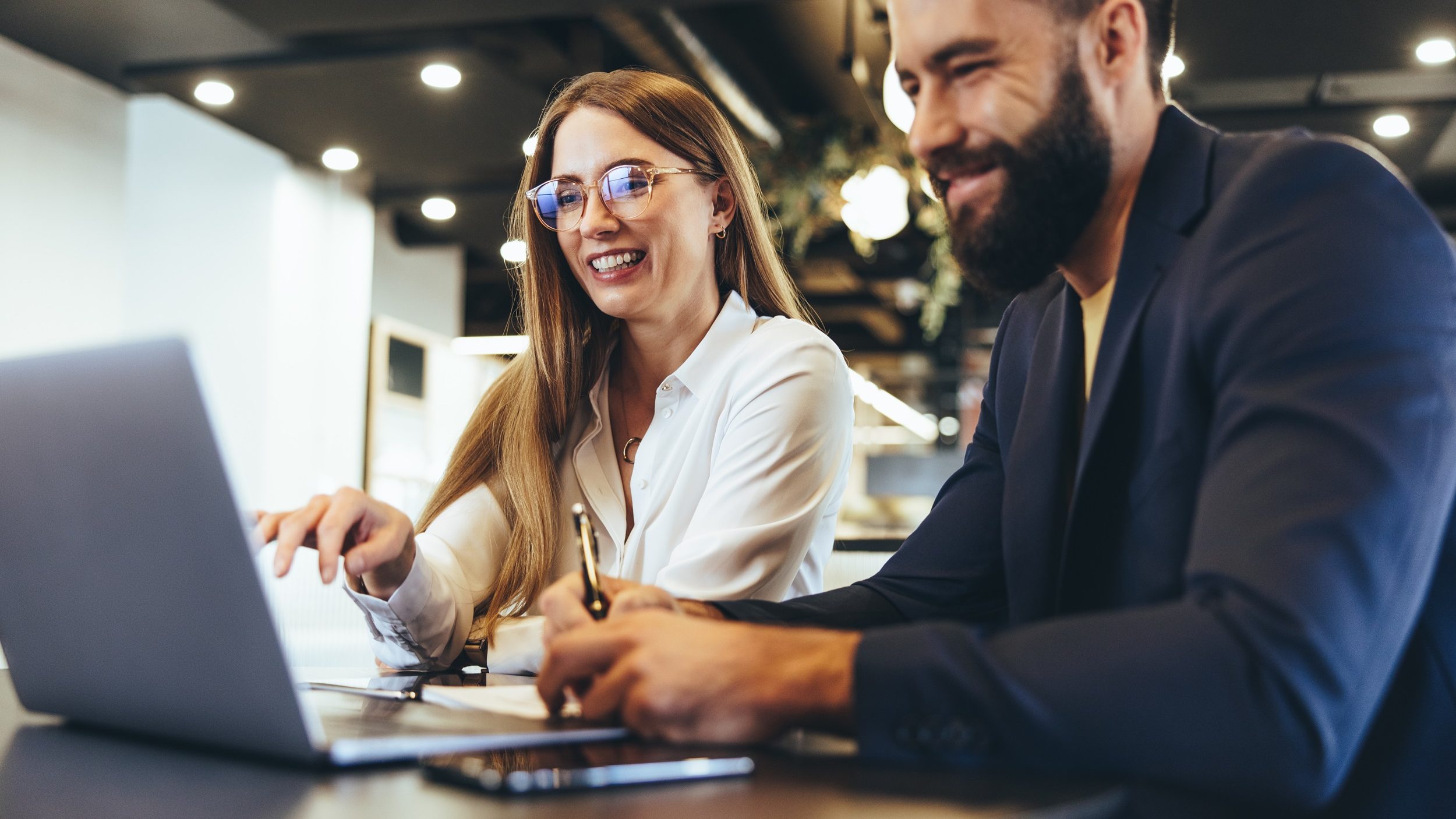 Eine junge Frau und ein junger Mann sitzen lächelnd vor einem Laptop.