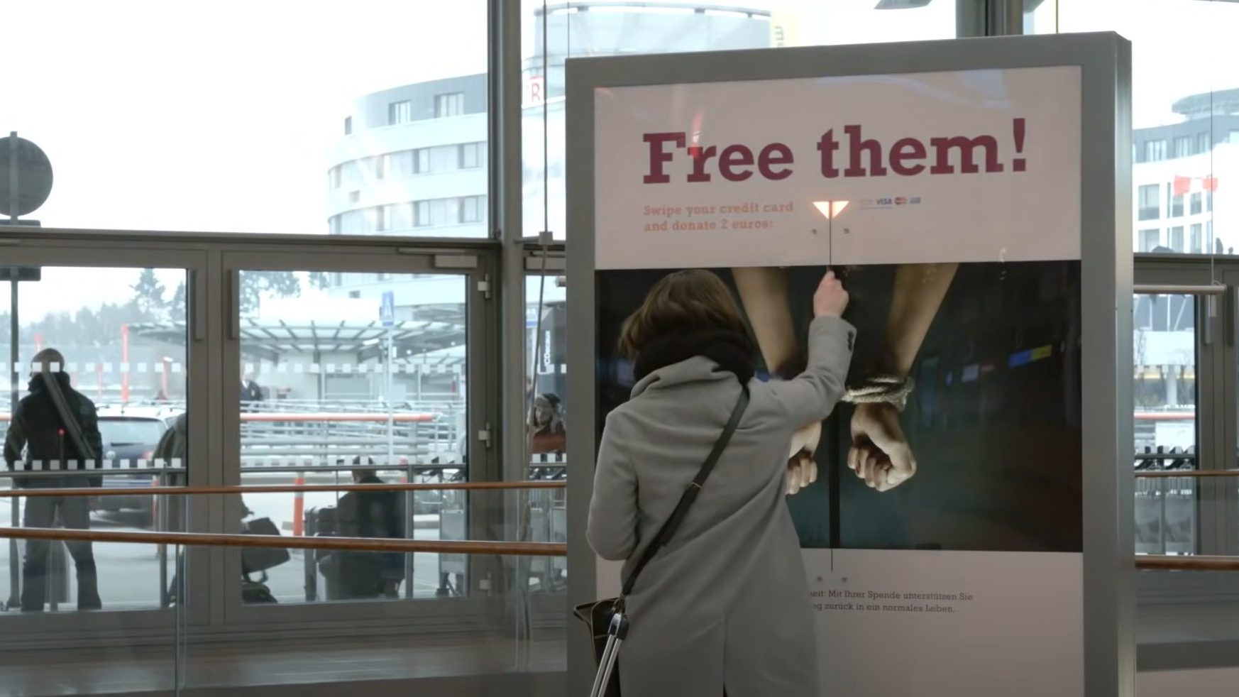 Eine Frau steht vor einer Säule und hält ihre Karte hin. Auf der Säule steht "Free them"