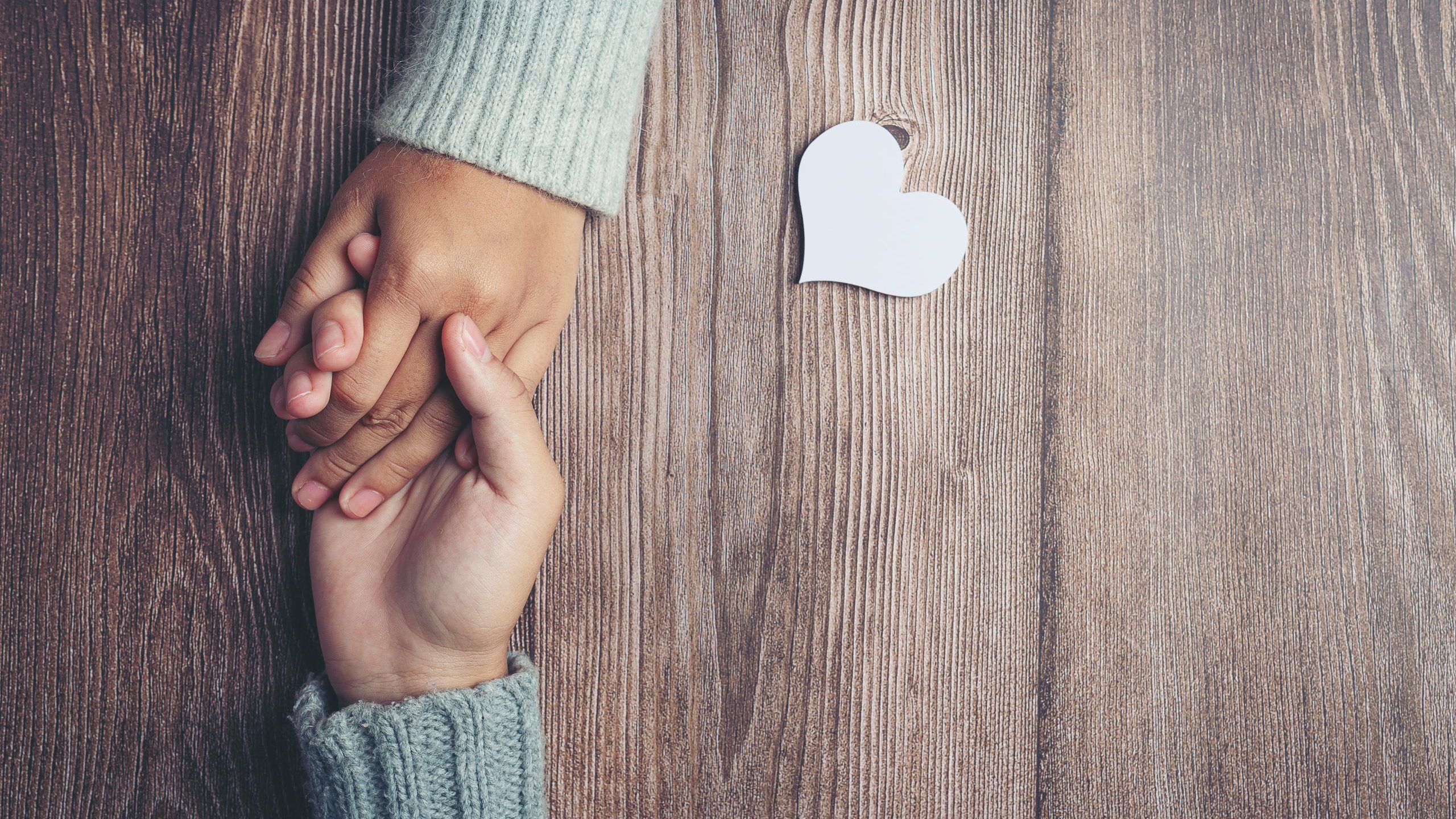 Zwei sich haltende Hände und ein Herz, das auf einem Tisch liegt