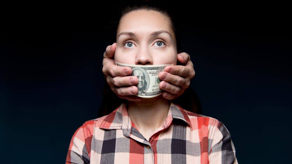 Eine Frau, der mit einem Geldschein der Mund zugehalten wird.
