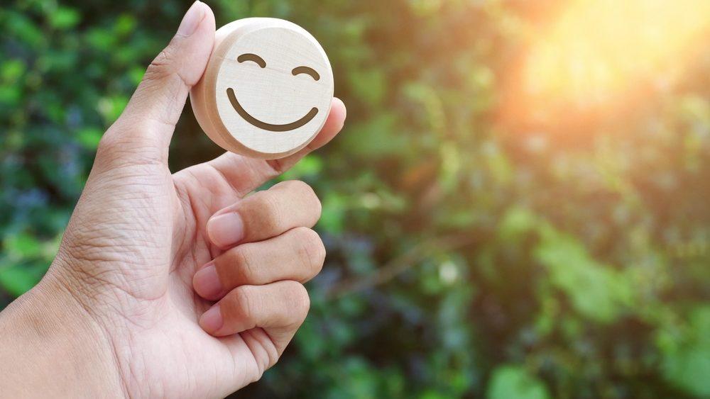 Eine Hand hält einen glücklichen Smiley aus Holz